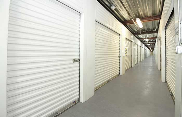 Indoor storage units with roll-up doors in well lit hallway.