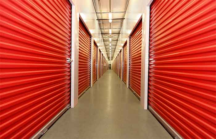 Indoor storage units with roll-up doors in a long hallway.