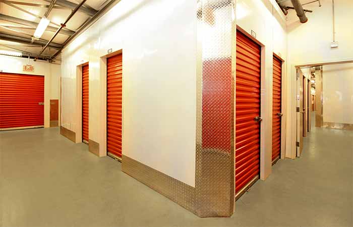 Small indoor storage units with roll-up doors in a well lit hallway.