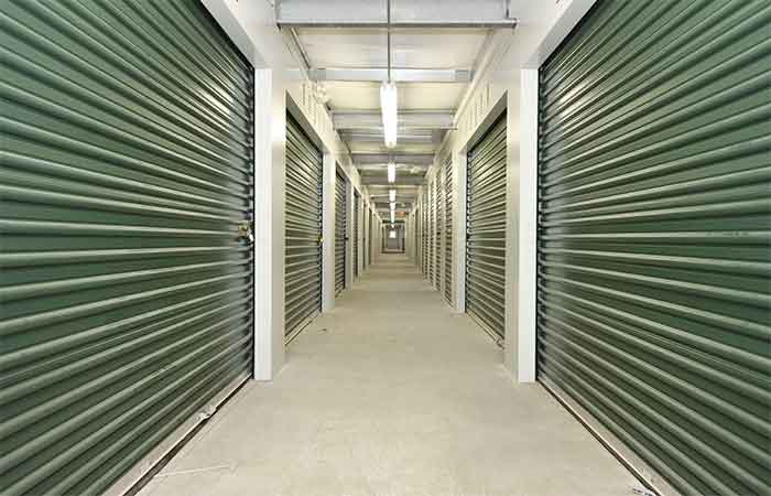 Large indoor storage units with roll-up doors in a well-lit hallway.