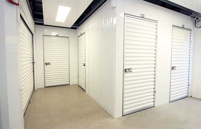 Indoor climate controlled storage units with swing doors, in a well-lit hallway.